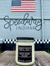 Load image into Gallery viewer, Back home again candle in clear jar with black label and lid. Shown in front of builidng with "Speedway, IN" painted and an American flag. True summer candle!