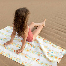 Load image into Gallery viewer, Little girl sitting on the Dock &amp; Bay Quick Dry Kids Towel on the beach.  
