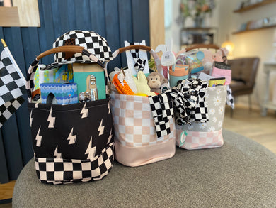 Easter baskets in 3 different patterns: black and white checkered bottom with black background and white lightening bolts on top; Light tan and white checkered with tan bottom; light pink and white checkered bottom with light tan top and white daisies.  Each as leather strap on top of handle. 