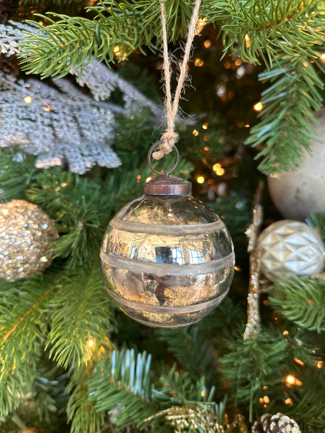 A vintage gold modern ornament with stripes. The ornament is round and has a gold-colored base. The stripes are horizontal and are in different shades of gold. The ornament is hanging from a twine string.