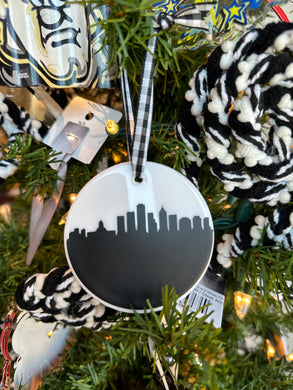 White round ceramic ornament with the Indianapolis skyline in black and hung with a black and white checkered ribbon. 