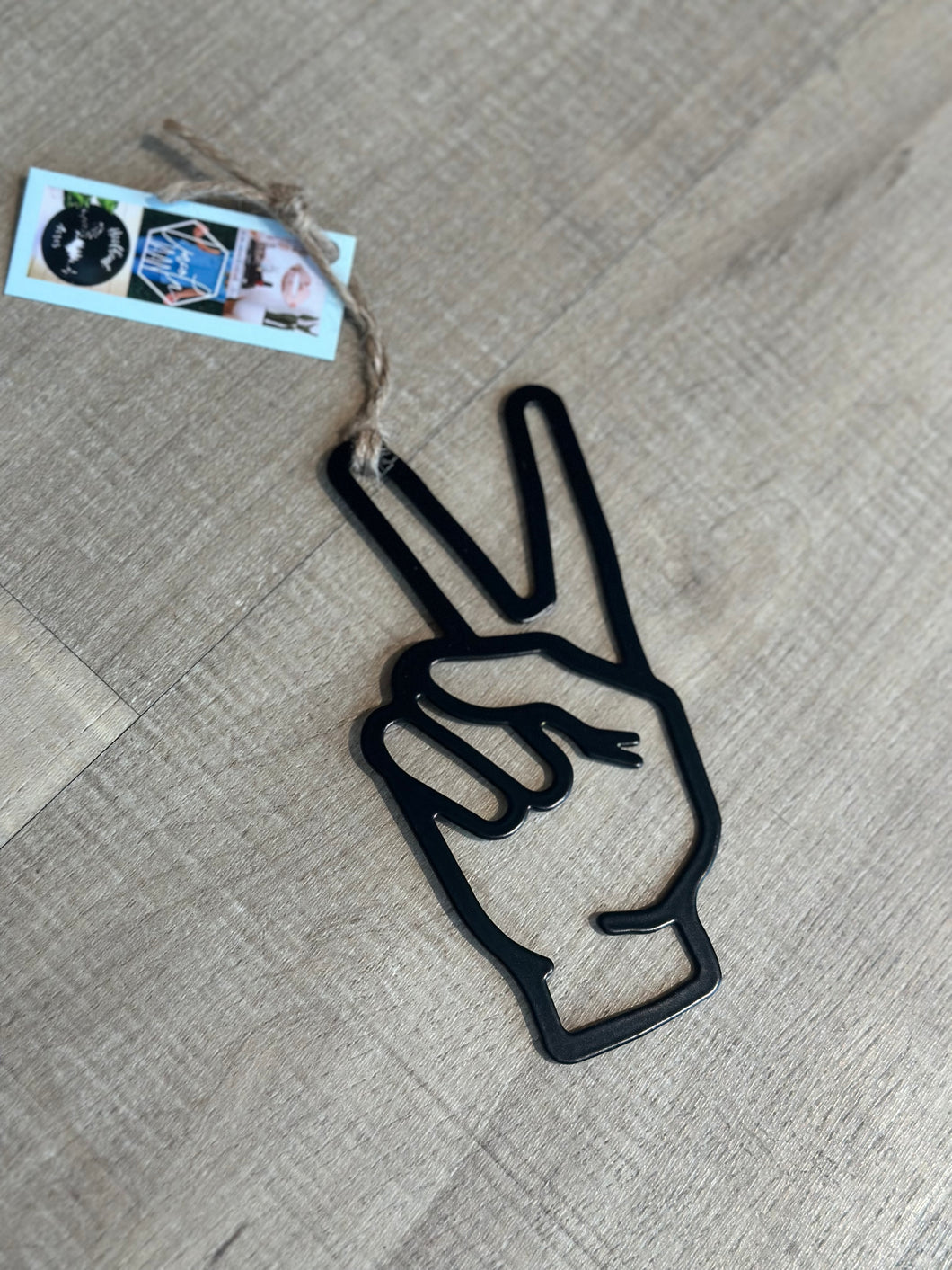 Black metal peace sign ornament.  Cutout hand showing 2 fingers up--a sign of peace.  Hung with twine. 