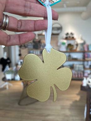 Gold metal shamrock shaped ornament with white ribbon for hanging. 