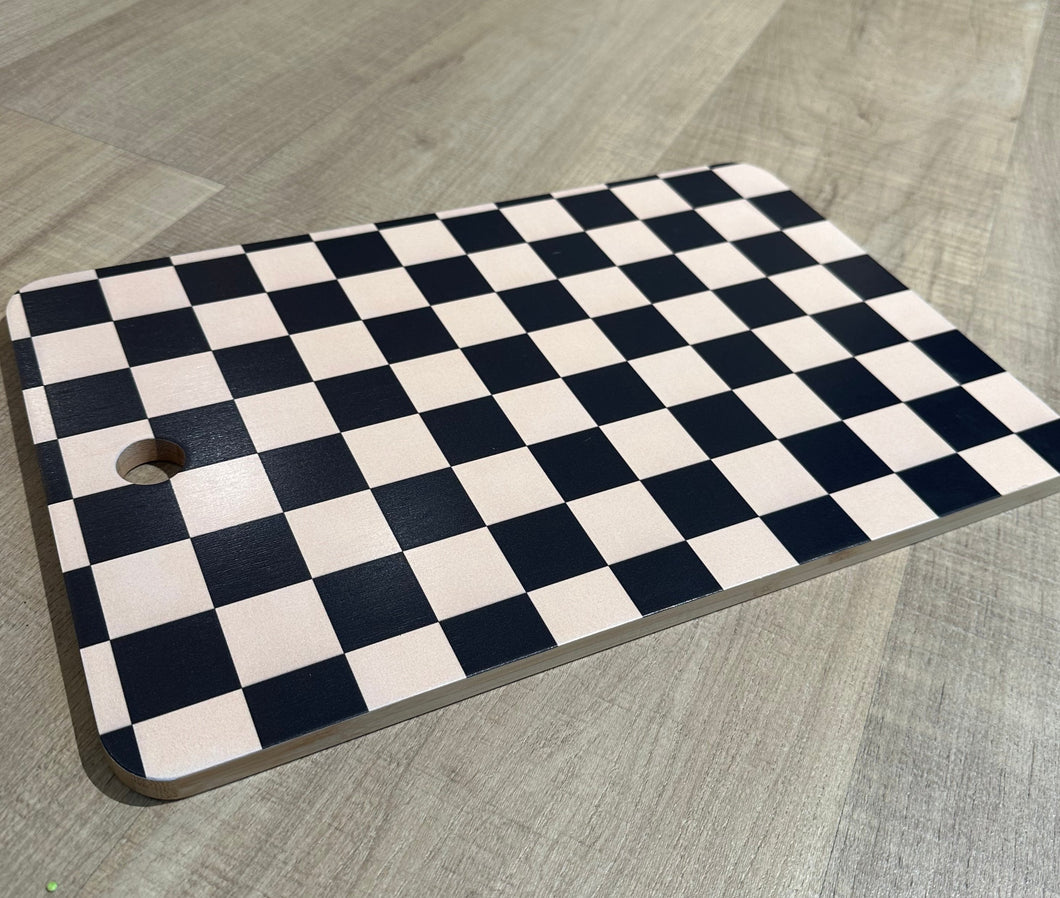 Black and cream checkered cutting board with hole to hang for display. 
