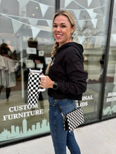 Load image into Gallery viewer, Model has crossbody black and white checkered purse/wristlet on.  Also holding our checkered tumbler. 
