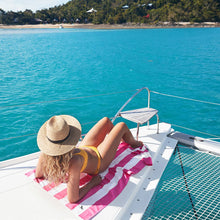 Load image into Gallery viewer, Woman on boat laying on Extra Large Dock &amp; Bay Quick Dry Towel in Phi Phi Pink. 

