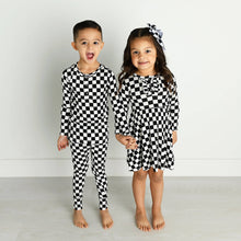 Load image into Gallery viewer, Little girl with checkered hair bow in hair and checkered dress and little boy with checkered pajamas on. 
