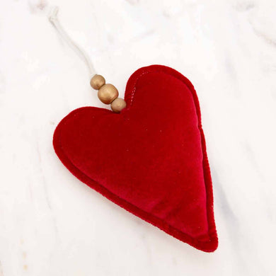 A charming little plush ornament in the shape of a red heart, adorned with a string hanger strung with three wooden beads.