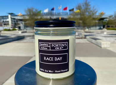 Race Day 7.5 oz soy candle shown in clear jar with black label and black lid.  Sitting right in front of the iconic Indianapolis Motor Speedway! 